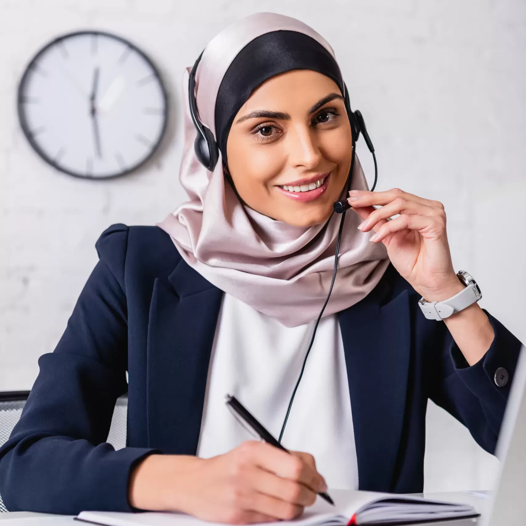 happy arabian interpreter in headset holding pen near notebook and digital translator with uae flag emblem on blurred foreground