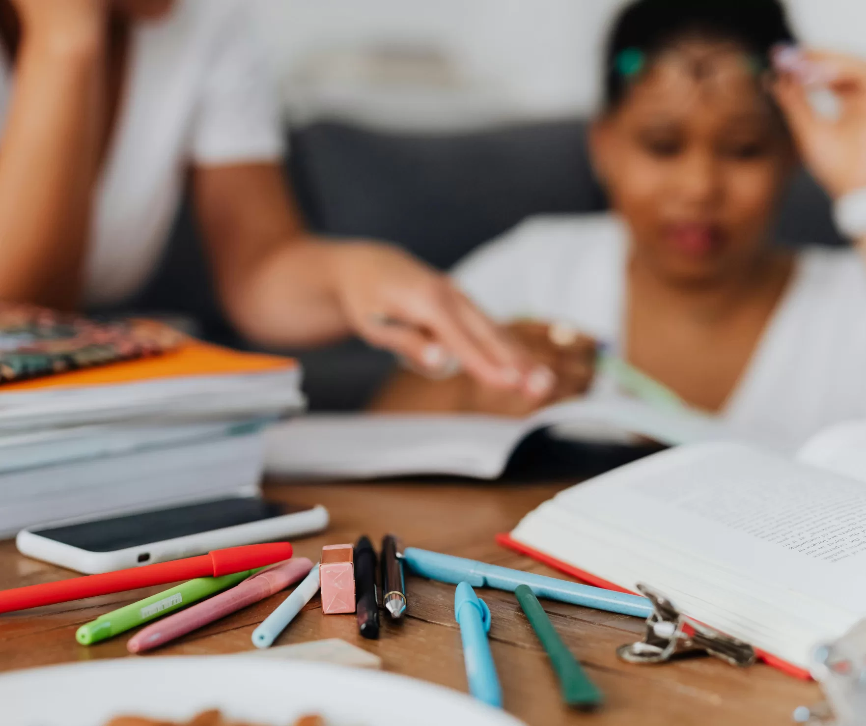 A table full of pens and books with multiple students surrounding the table and reading books.